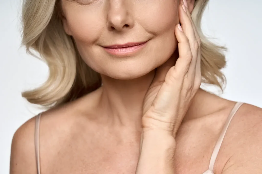 Close-up of a mature woman touching the side of her face and neck with one hand.